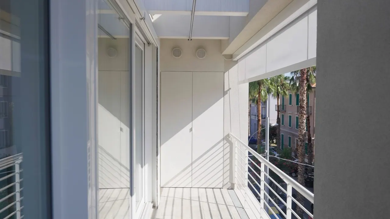 Balcone chiuso con lo scorrevole e la tenda, affacciato su una via con le palme